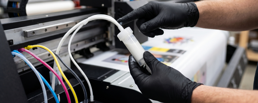  Gloved hands handling a white ink cartridge on a DTF printer, with CMYK ink tubes visible, highlighting white ink as the most critical component in a DTF system.
